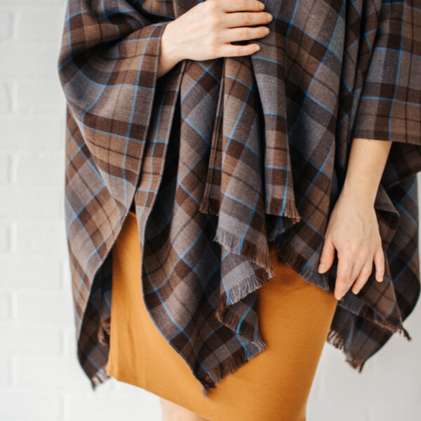 A woman wearing an OUTLANDER Wrap Premium Lambswool Tartan in brown plaid, a premium lambswool tartan poncho.